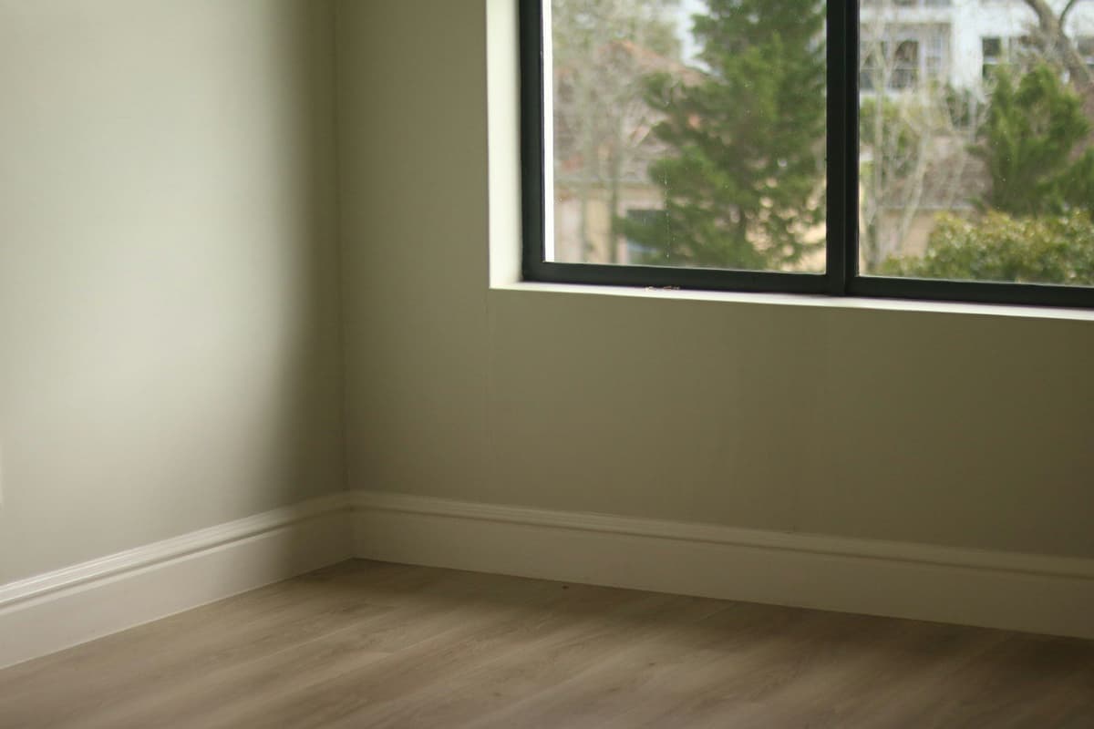 Empty room with light green walls, wooden floor, and window